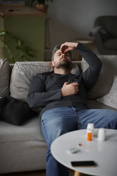 A handsome man sits back on a couch, showing signs of discomfort while surrounded by everyday life. — Stock Photo