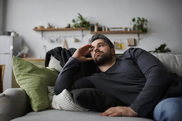 Un bell'uomo è sdraiato su un divano morbido, guardando in lontananza mentre nel profondo del pensiero. — Foto stock