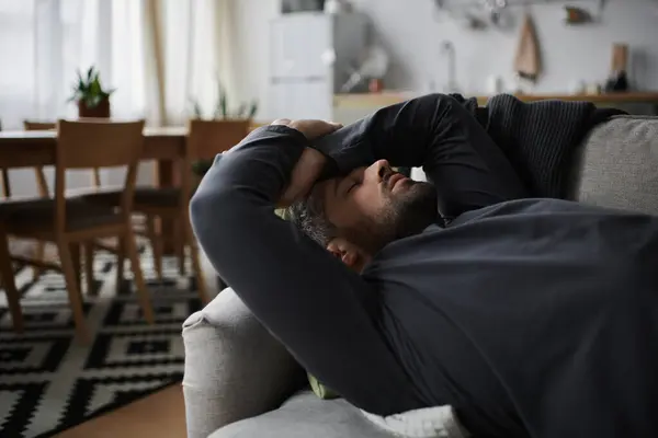 A handsome man lies on a couch, enjoying a tranquil afternoon in a cozy living space. — Stock Photo