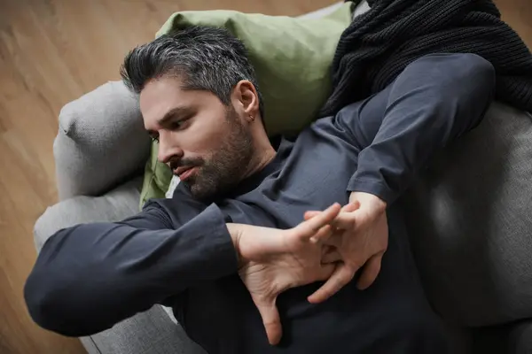 Um homem bonito reclina confortavelmente em um sofá, esticando os braços em um espaço tranquilo. — Fotografia de Stock