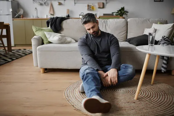 A handsome man sits thoughtfully on the floor of his inviting living space, lost in reflection. — Stock Photo