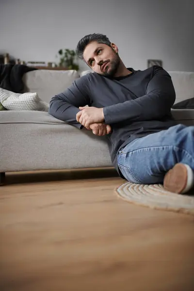 A handsome man sits on the floor, lost in thought while relaxing in a comfortable living room. — Stock Photo