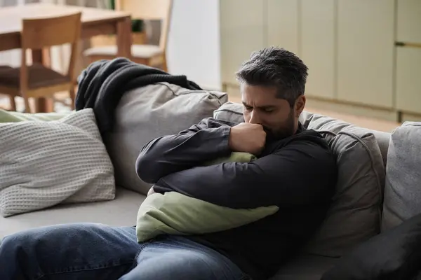 A man rests on a couch, holding a pillow close while lost in thought in a serene living space. — Stock Photo