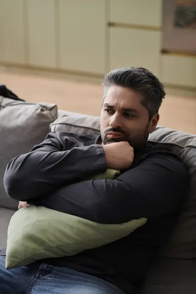 A handsome man sits thoughtfully on the couch, holding a pillow close during a serene afternoon. — Stock Photo