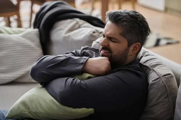 A handsome man sits comfortably on a couch, holding a green pillow while enjoying a peaceful moment. — Stock Photo