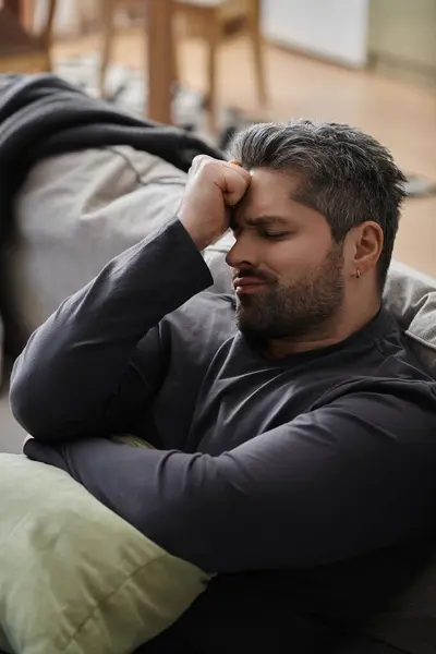 A handsome man rests his head on his hand, appearing contemplative and relaxed on a cozy couch. — Stock Photo