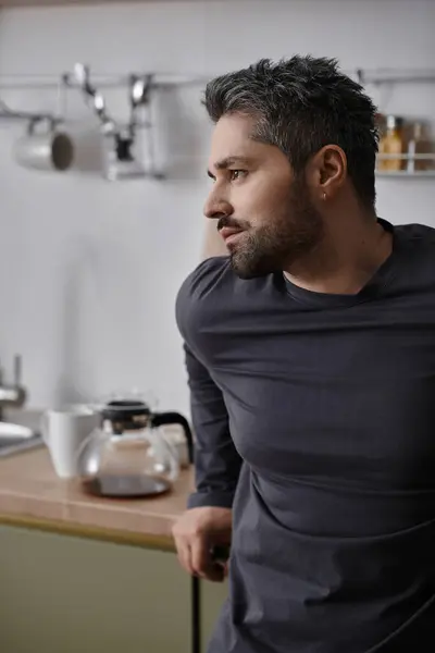 A handsome man leans against a kitchen counter, savoring a peaceful morning ritual. — Stock Photo