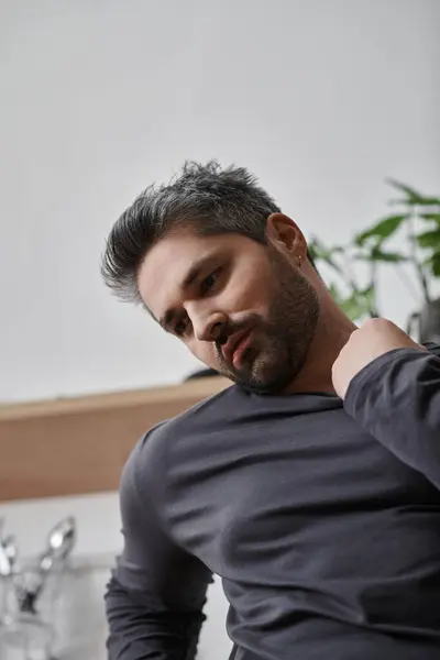 A handsome man sits at home, showcasing a thoughtful moment surrounded by greenery and elegance. — Stock Photo