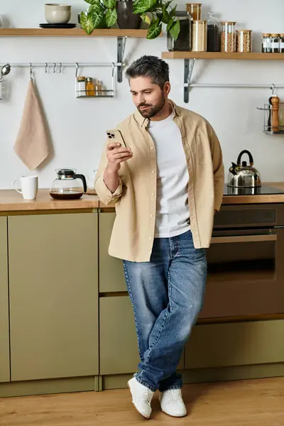 Un bell'uomo controlla casualmente il suo telefono in una cucina moderna, godendo di un momento di relax. — Stock Photo