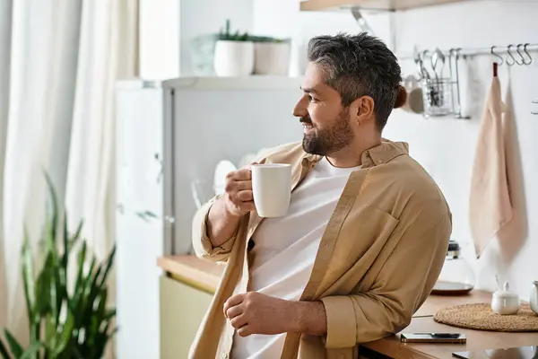 A handsome man leans against a kitchen counter, sipping coffee and enjoying a peaceful moment. — Stock Photo