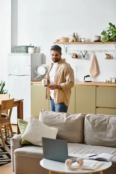 A handsome man stands in a bright kitchen, savoring a cup of coffee while enjoying a serene morning. — Stock Photo