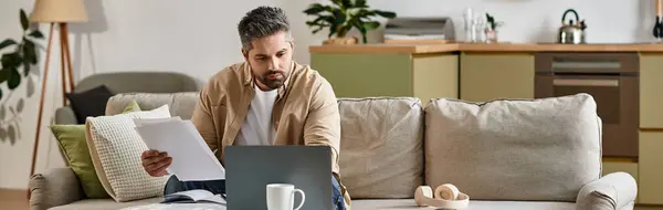 A handsome man is focused on his laptop, sitting comfortably on a sofa surrounded by greenery. — Stock Photo