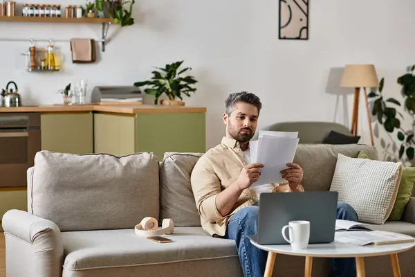 A handsome man sits comfortably reading documents in a stylish living room filled with greenery. — Stock Photo