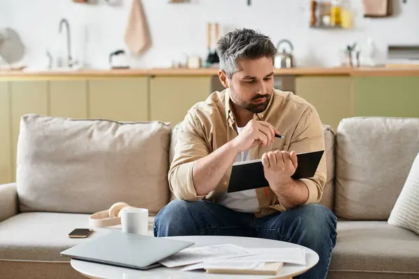 A handsome man meticulously writes notes while seated in a cozy living space. — Stock Photo