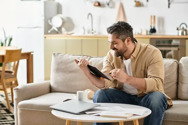 Ein Herr entspannt sich auf einem Sofa und lächelt, während er bei Tageslicht ein Buch liest. — Stockfoto