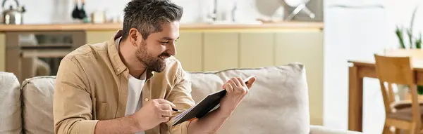 Um homem alegre sorri enquanto esboça em um tablet, cercado por um ambiente acolhedor e moderno. — Fotografia de Stock