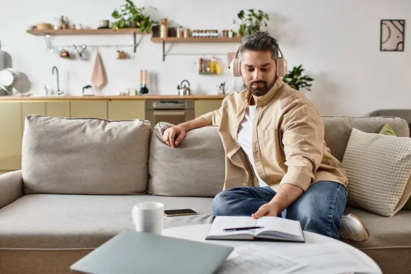 A handsome man enjoys his time at home, seated on a cozy couch as he flips through a book. — Stock Photo