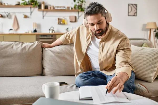 Focused man engaged in studying with headphones on in a stylish and inviting living space. — Stock Photo