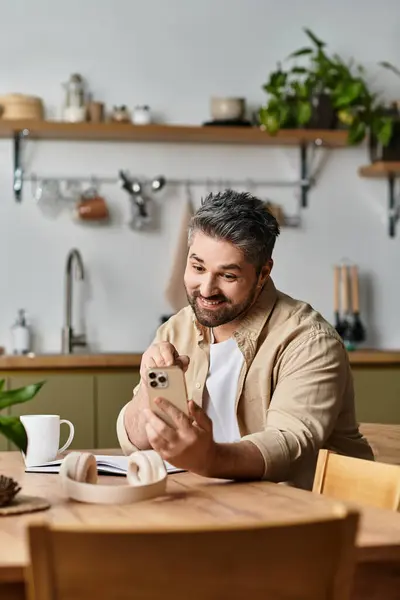 A handsome man enjoys a lively chat on his phone surrounded by a warm kitchen atmosphere. — Stock Photo