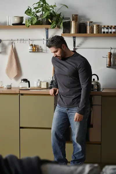 A handsome man stands thoughtfully in a warm kitchen with a modern design, reflecting on his day. — Stock Photo