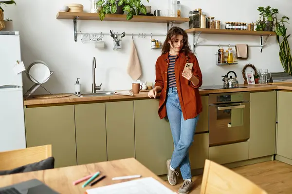 Una giovane donna si trova in una cucina calda, contemplando i suoi sentimenti mentre guarda il suo telefono. — Foto stock