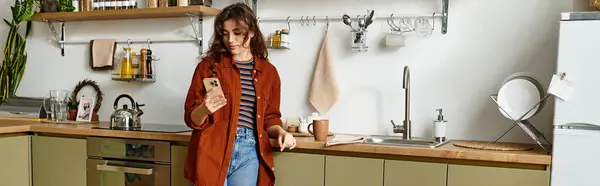 Жінка стоїть одна на сонячній кухні, втрачена під час перевірки телефону. — Stock Photo