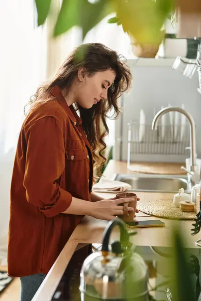 A woman stands quietly in a sunlit kitchen, holding a warm cup, lost in her thoughts and emotions. — Stock Photo