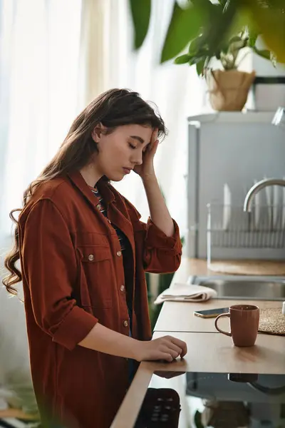 A woman stands in a kitchen, resting her forehead on her hand, lost in deep thoughts. — Stock Photo