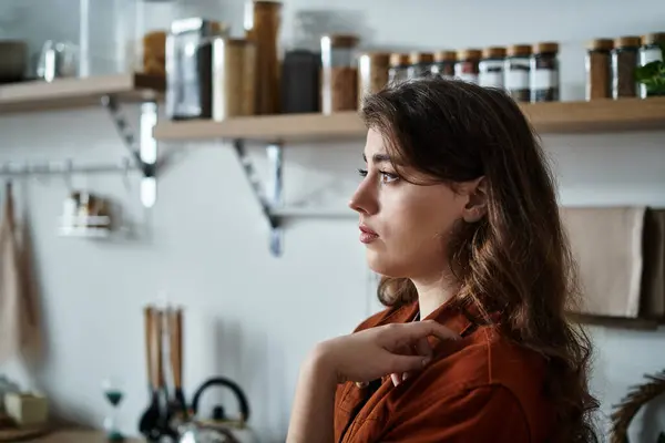 A woman stands thoughtfully in a warm kitchen, grappling with feelings of sadness and reflection. — Stock Photo