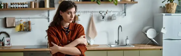 A woman stands in a minimalist kitchen, arms wrapped around herself, lost in contemplation. — Stock Photo