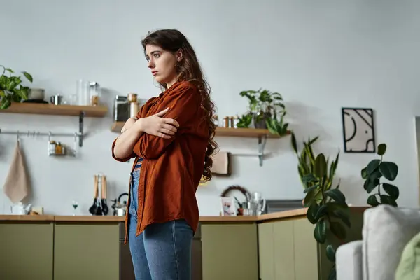 A woman with long hair stands thoughtfully in a warm kitchen, expressing her battle with sadness. — Stock Photo