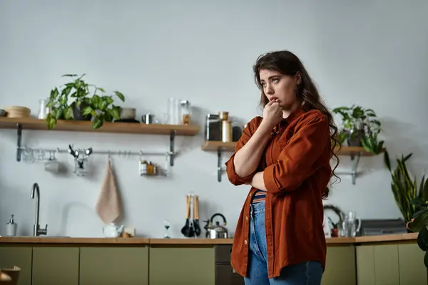 A woman stands thoughtfully in a serene kitchen, surrounded by greenery, reflecting on her feelings. — Stock Photo