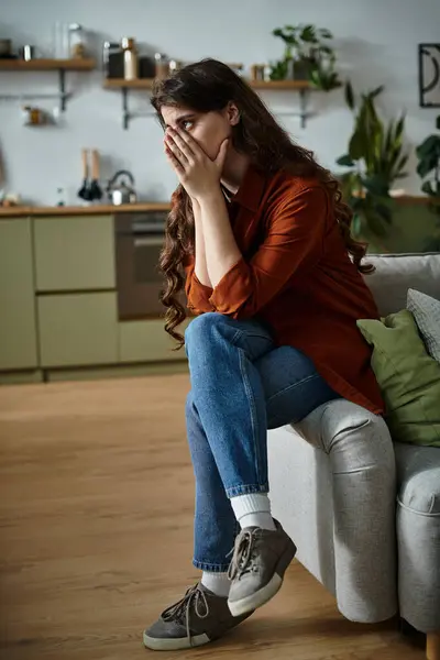 Женщина сидит на диване, переполненная эмоциями в своей стильной кухне. — стоковое фото
