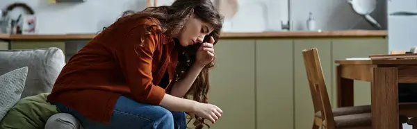 In a cozy living area, a woman sits on a sofa with her head bowed, lost in thought and emotion. — Stock Photo