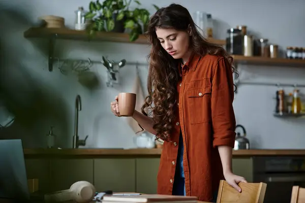 A woman contemplates her thoughts while holding a warm beverage in a cozy kitchen. — Stock Photo