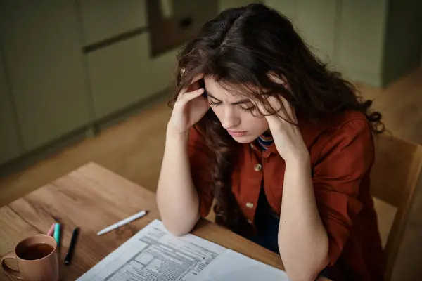 Una mujer se sienta en una mesa de madera, perdida en el pensamiento, lidiando con sus sentimientos de desesperación. — Stock Photo