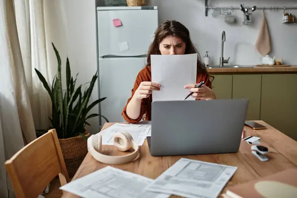 A woman examines documents while sitting at her desk, feeling the weight of her worries. — Stock Photo
