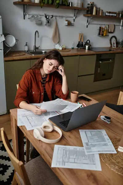 A woman sits at a kitchen table overwhelmed by paperwork and feelings of sadness. — Stock Photo