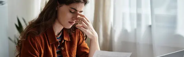 A woman sits at a desk in a bright room, her face reflecting deep thought and sadness as she reads. — Stock Photo
