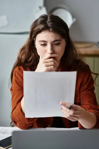 A woman sits at a kitchen table, deeply focused on papers, showing emotional conflict. — Stock Photo