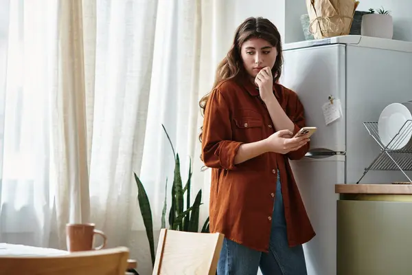In a softly lit kitchen, a woman gazes at her phone, lost in swirling emotions. — Stock Photo