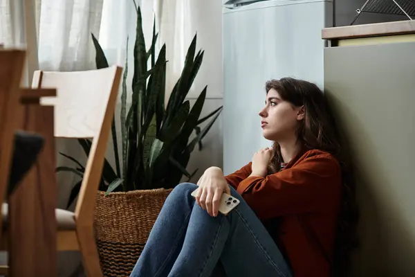A woman seated on the floor near a plant, lost in thought while grappling with her feelings. — Stock Photo