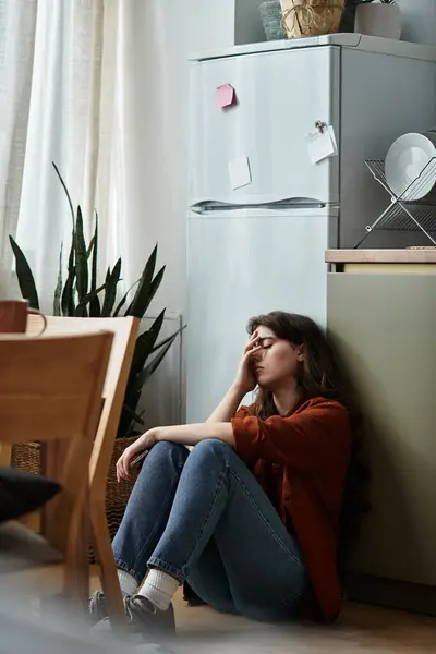 En una acogedora cocina, una mujer se apoya contra la pared, su rostro muestra confusión interior y tristeza. - foto de stock