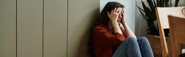 Женщина в уютной комнате сидит у стены, затерявшись в своих мыслях, олицетворяя тяжесть печали. — стоковое фото