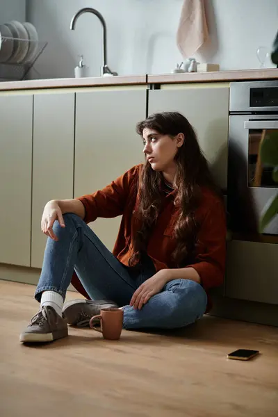 Une femme assise sur le sol de la cuisine, engloutie dans la tristesse et la solitude. — Photo de stock