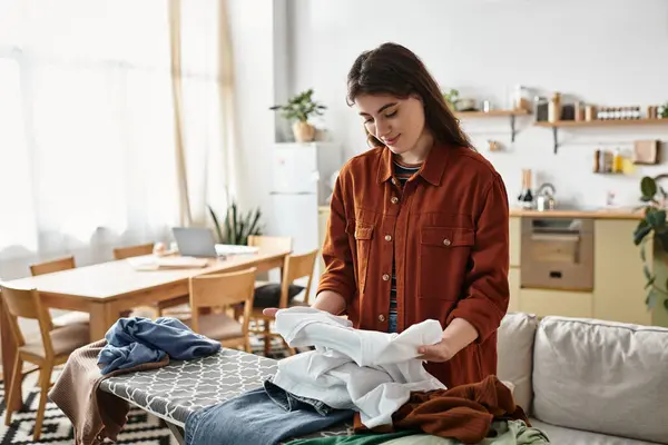 Eine Frau stellt sich ihren Emotionen, während sie Kleider in einem gemütlichen, personalisierten Raum faltet. — Stockfoto