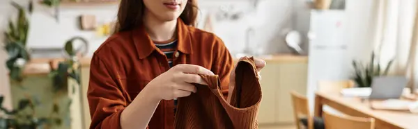 A woman sits in a warm kitchen, feeling the weight of her emotions as she examines her clothing. — Stock Photo