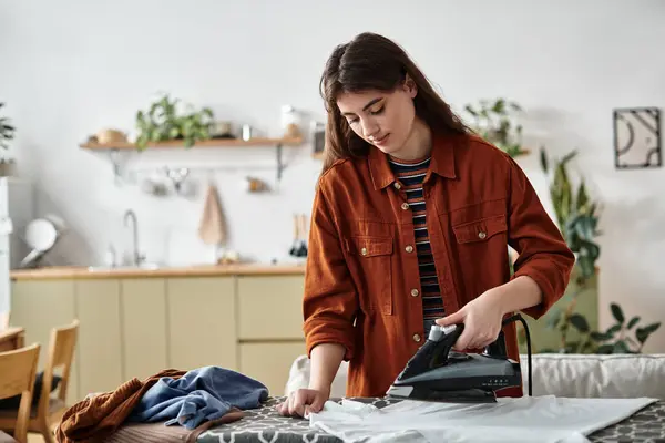 Une femme repasse tranquillement ses vêtements dans une cuisine lumineuse et minimaliste, perdue dans ses pensées et ses sentiments. — Photo de stock