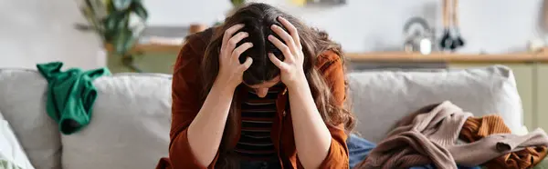 A woman sits on a couch, holding her head in distress, enveloped by feelings of sadness. — Stock Photo