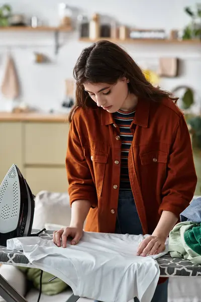 Uma mulher está focada em passar uma camisa branca em um espaço acolhedor, lutando contra emoções invisíveis. — Stock Photo